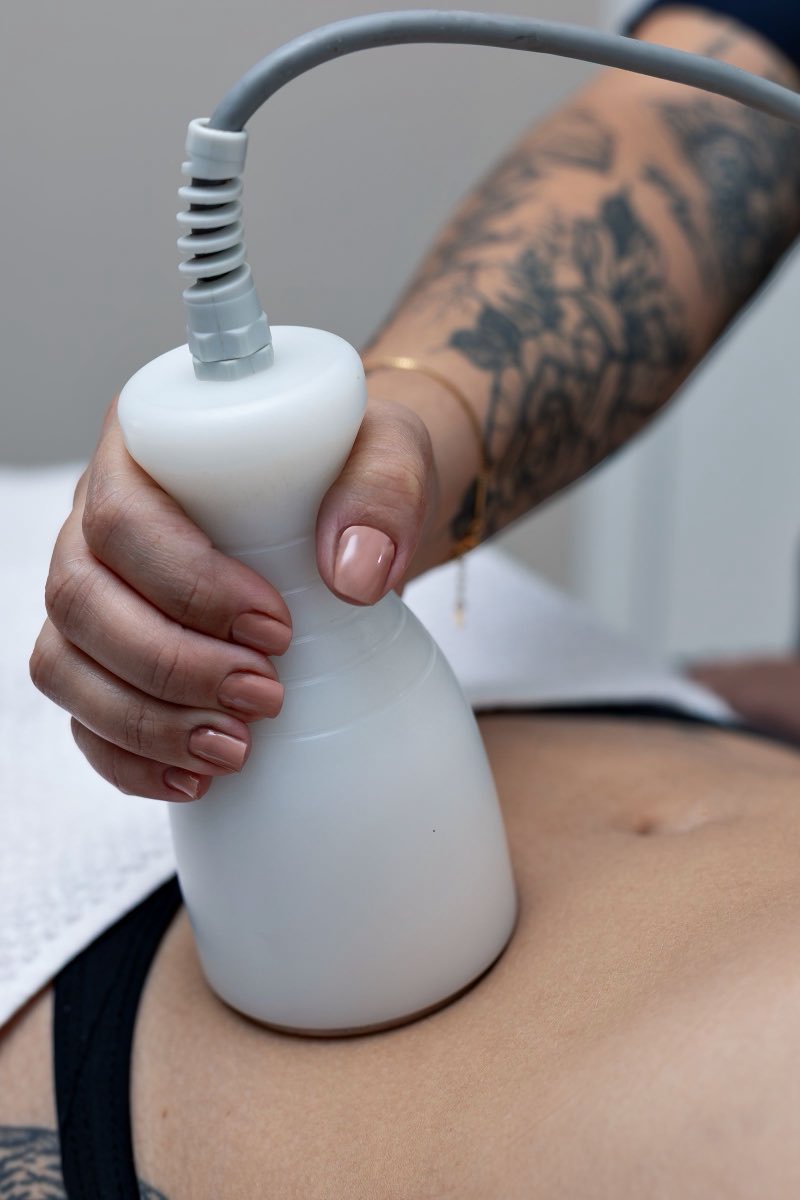 A close view of a hand guiding a smooth white treatment handpiece across a midriff, the cable running off to the left.