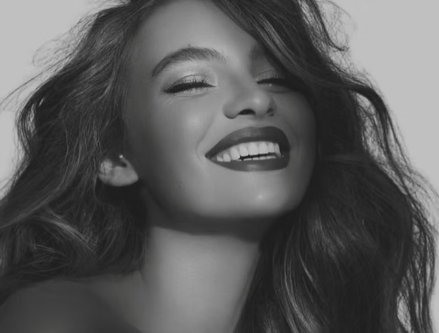 Black and white photograph of a woman laughing with her eyes closed, her hair caught mid movement.